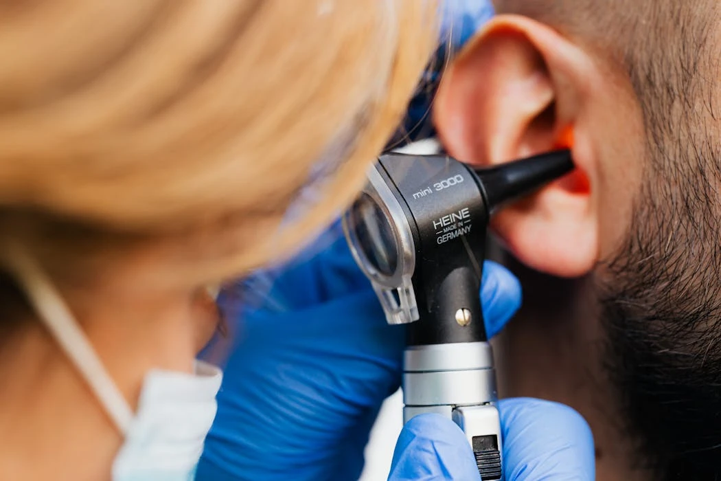 A medical professional examines a patient's ear using a Heine otoscope, highlighting healthcare quality.